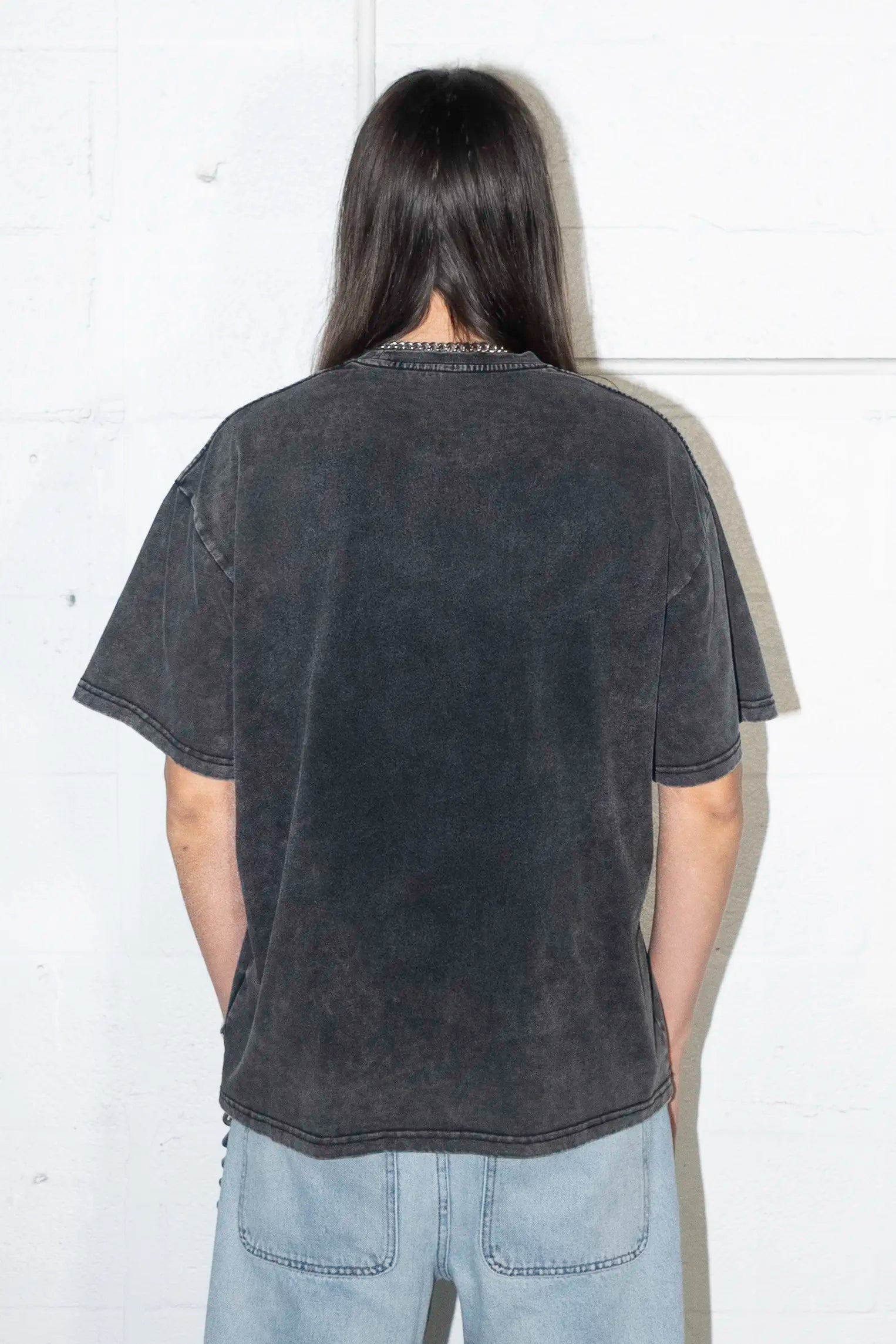 Person wearing a black with Parasite Label text and Slime Cat t-shirt and light blue jeans against a white wall