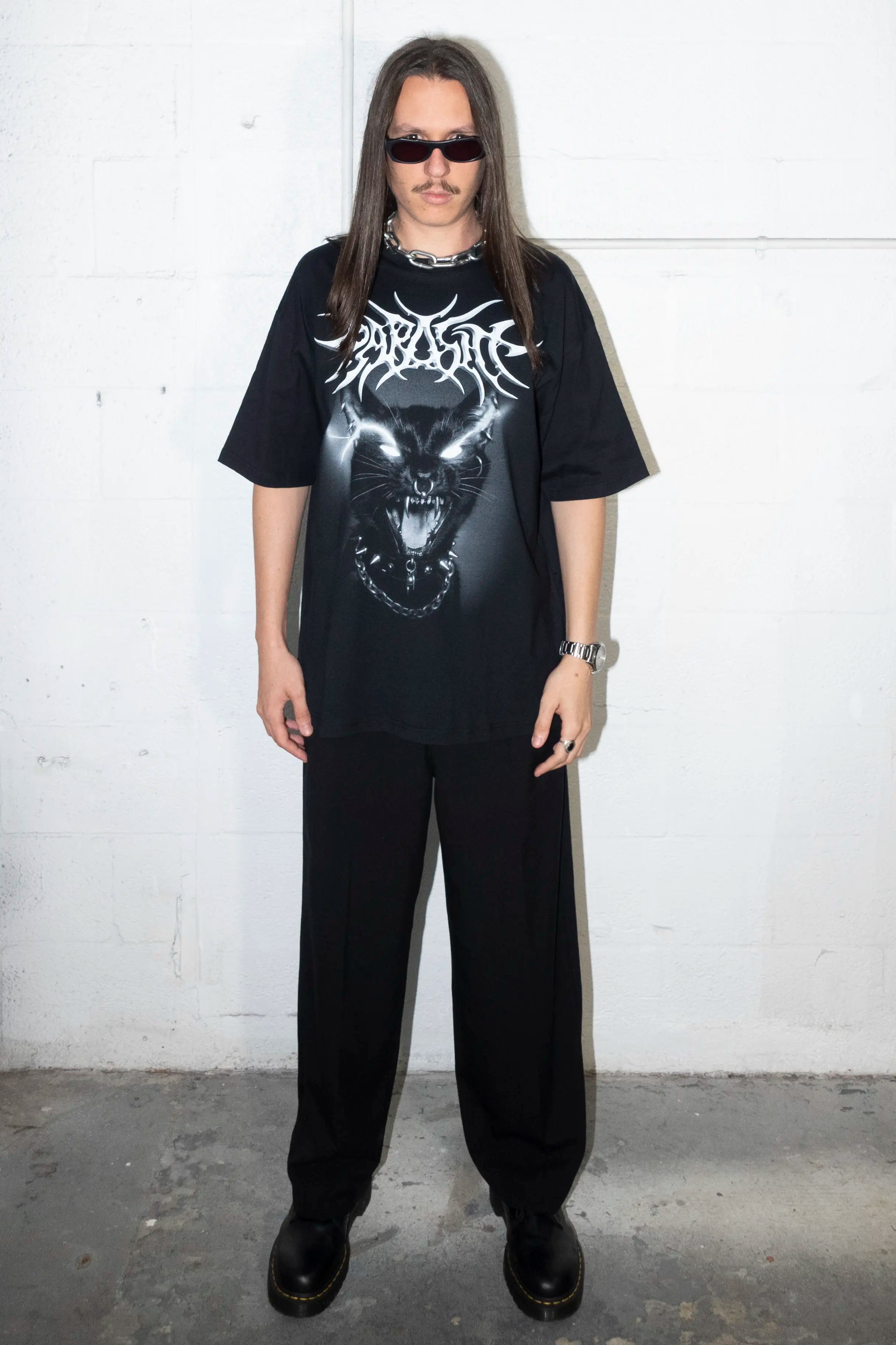 Person wearing a black graphic t-shirt with a Parasite Label screaming punk cat graphic design and text, standing against a white wall.