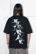 Person wearing a black t-shirt with a white spike chain link graphic design on the back against a white wall.