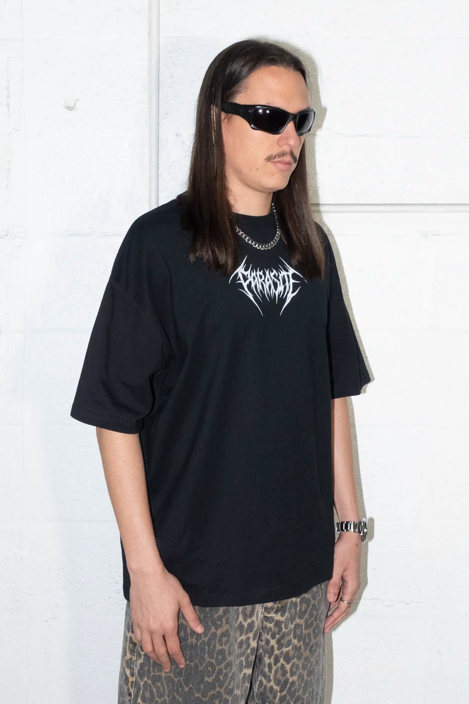Person wearing a black t-shirt with white Parasite Label text, standing against a white background.