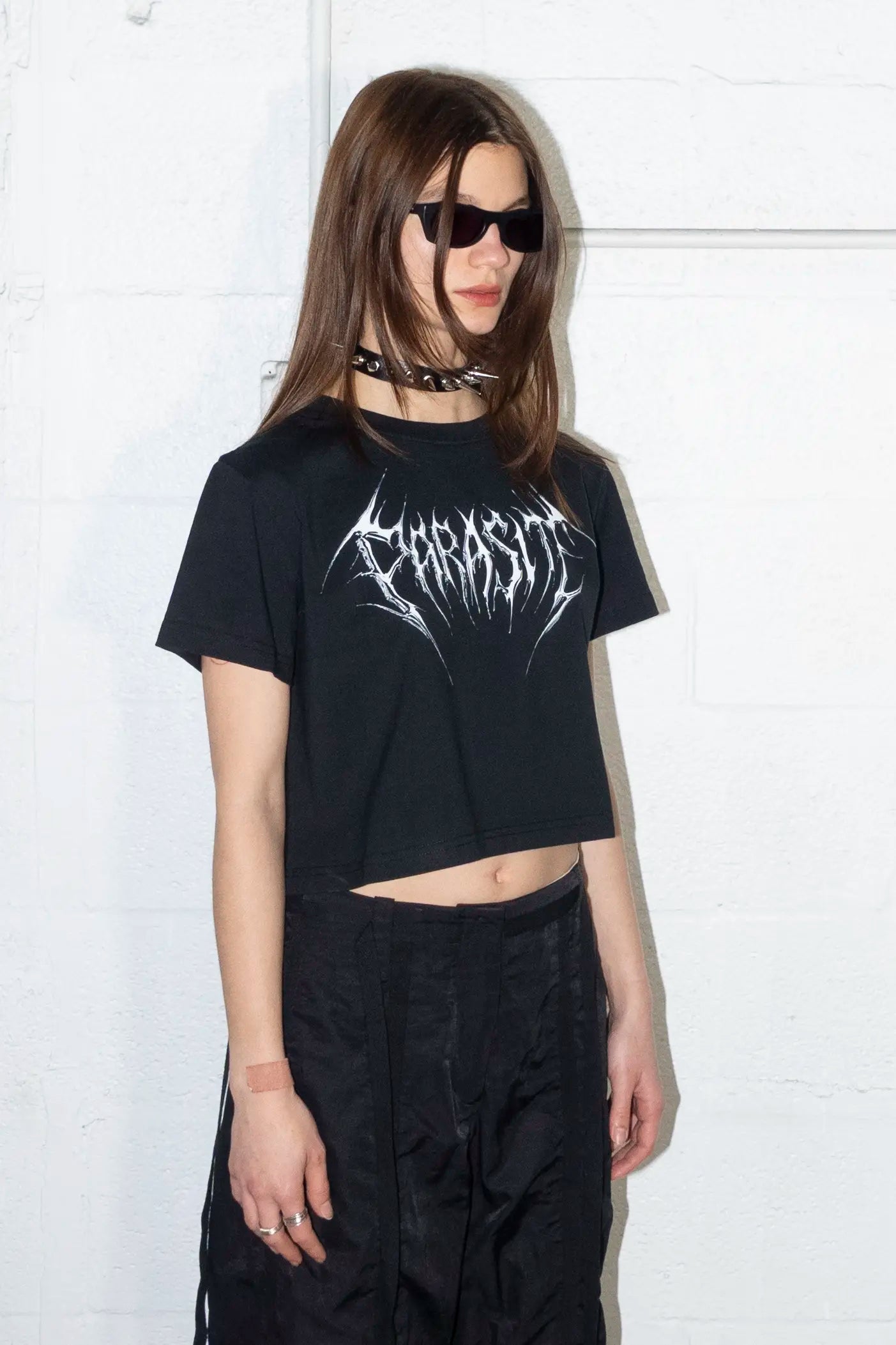 Person wearing a black t-shirt with Parasite Label chrome 3d text logo graphic design and sunglasses against a white background