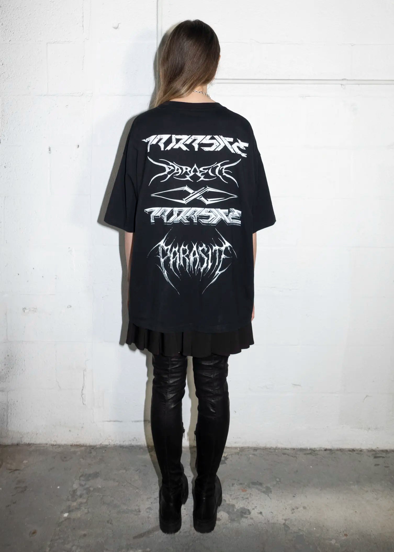 Person wearing a black t-shirt with white Parasite Label text against a white wall.