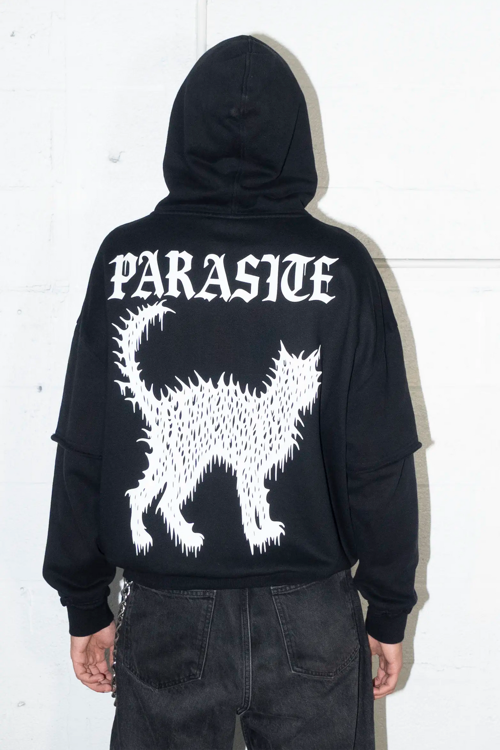 Person wearing a black hoodie with Parasite Label design on the back against a white background
