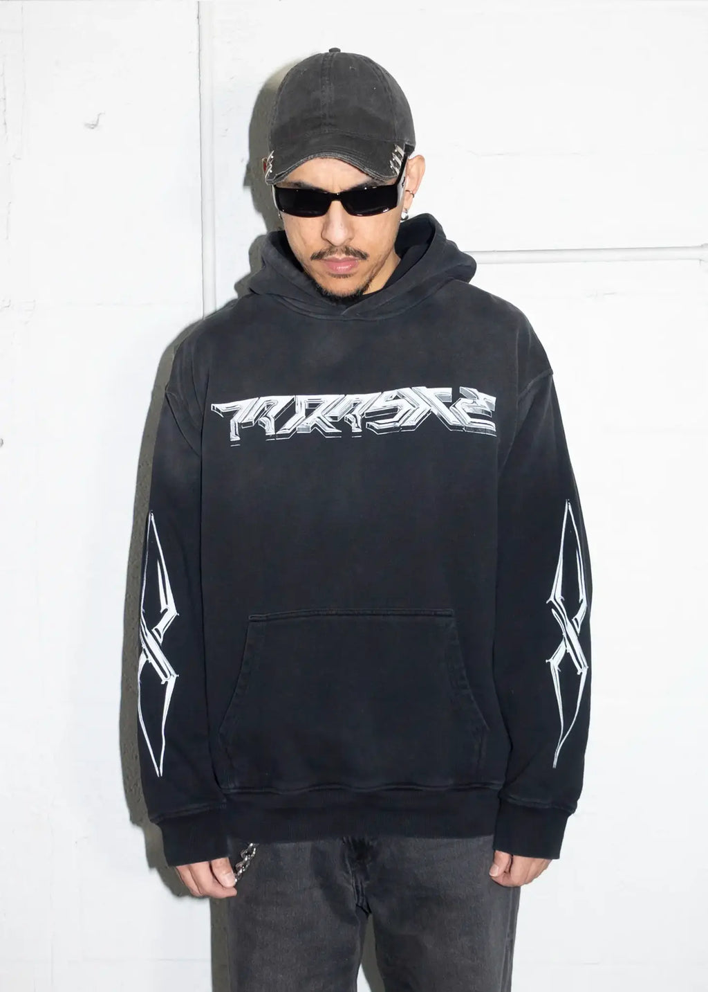 Person wearing a black hoodie with a chrome 3d Parasite Label logo and text, standing against a white background