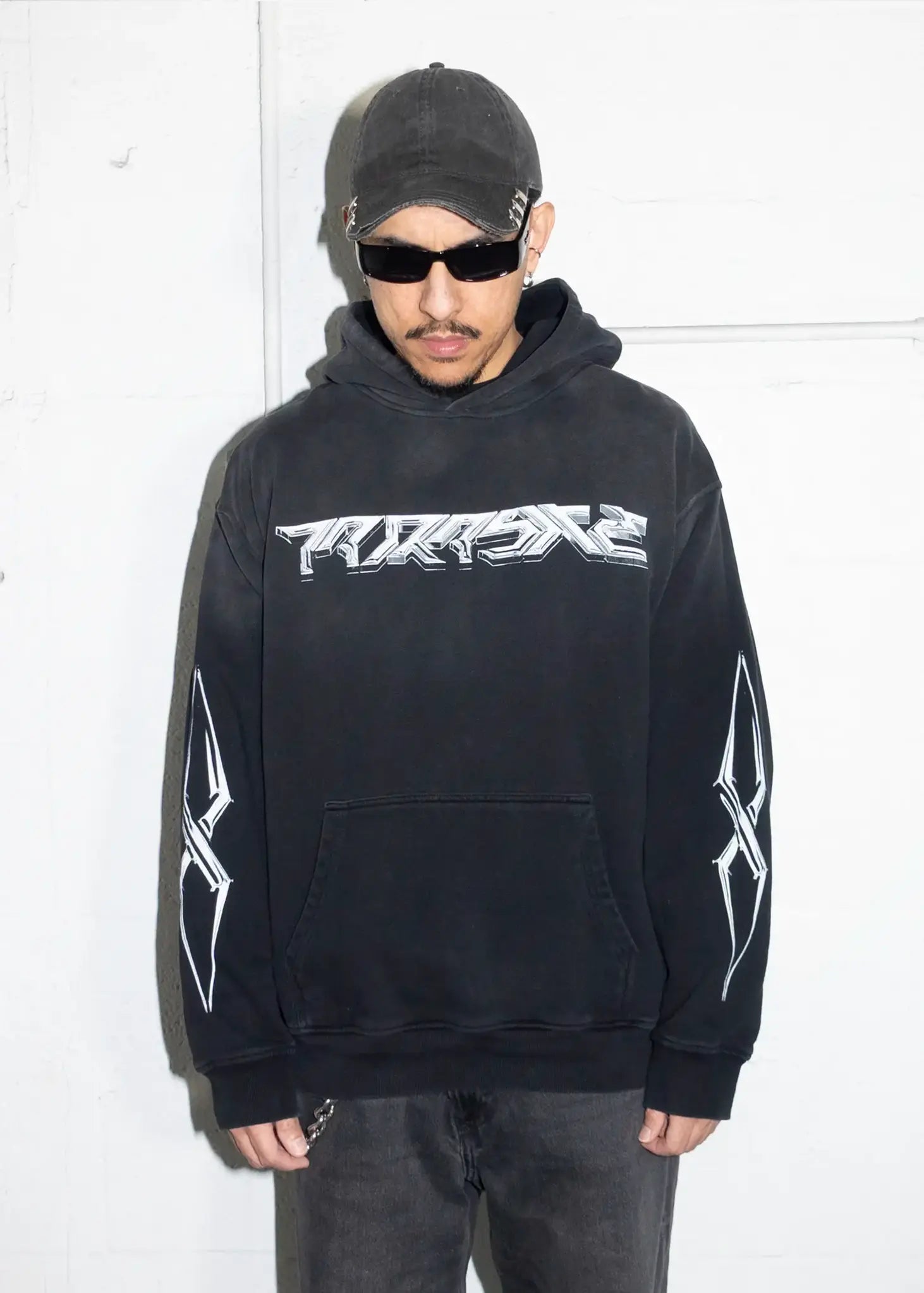 Person wearing a black hoodie with a logo and text, standing against a white background